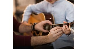 תלמיד מחזיק ולומד גיטרה, הידיים של המורה על הגיטרה כאשר הוא מראה לתלמיד איך לנגן